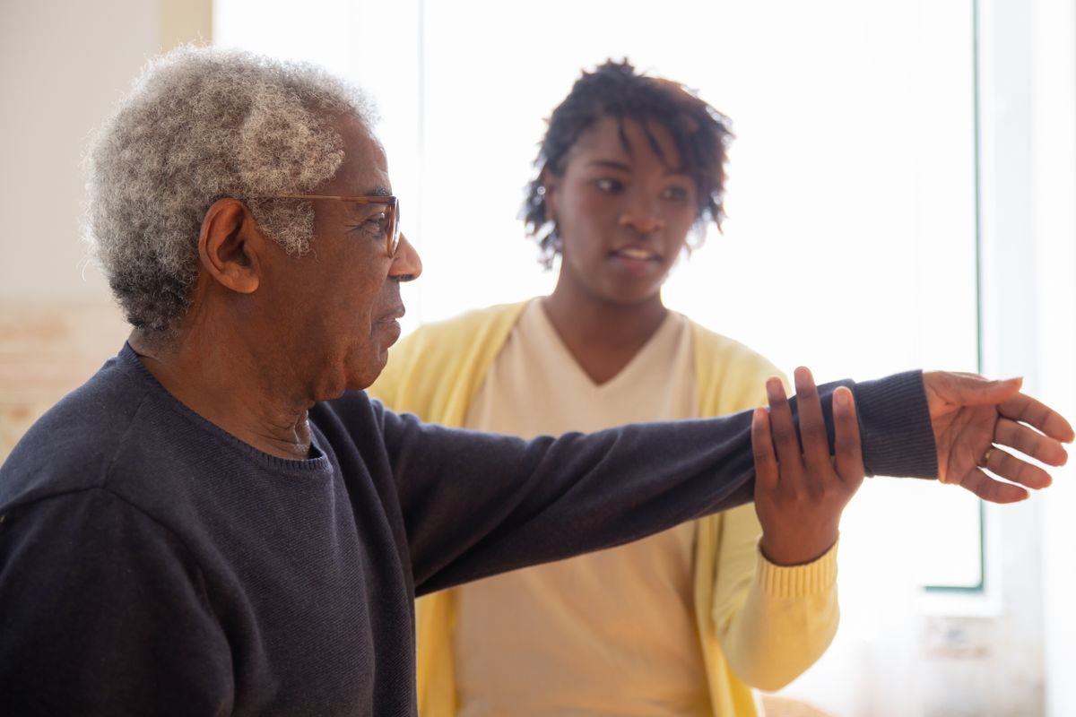 A companion supporting an older man during a stretching exercise at home